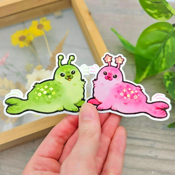 Picture of a hand holding two alien seal stickers.
